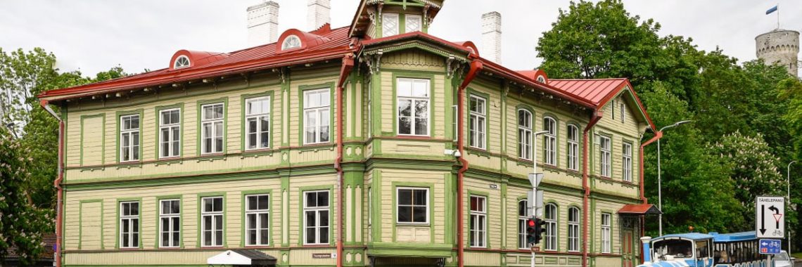 Charming green facade wooden building on a rainy day in Tallinn's Kassisaba, featuring urban life and tourist attractions.